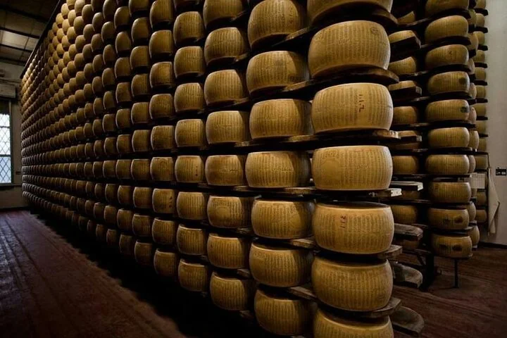Tall wooden shelves stacked with golden wheels of Parmigiano Reggiano in an aging room
