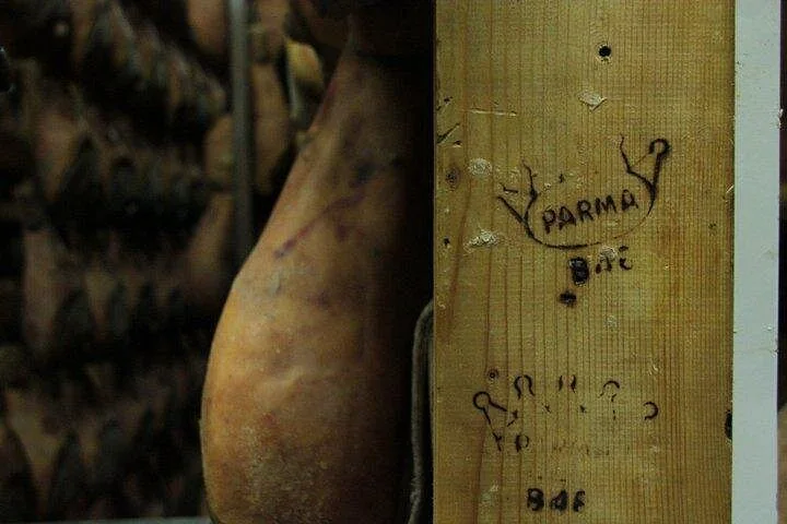 A cured ham hanging beside a wooden post marked with the crown and the word PARMA