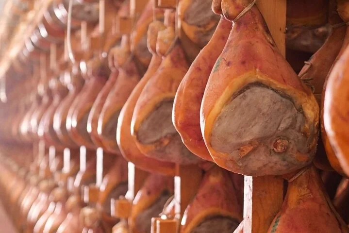 Nahaufnahme gereifter Schinken in Reihen, die mageren Schnittflächen mit einer blassgrauen Paste bedeckt