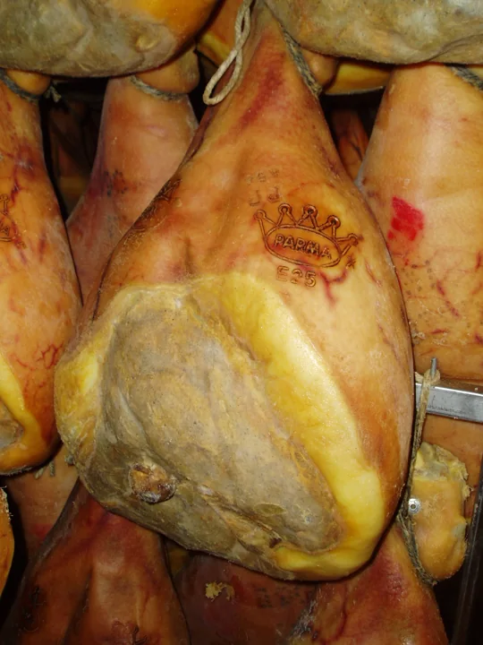 Cured Parma hams hanging close together, trimmed round, one showing the crown brand