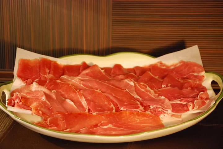 Dünne Prosciutto-Scheiben auf weißem Papier auf einer Platte mit grünem Rand